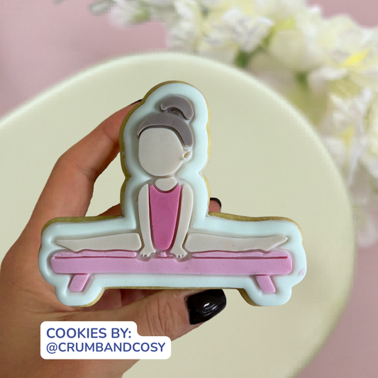 Cookie shaped like a person sitting on a bench with pink outfit, held by a hand against a light background.