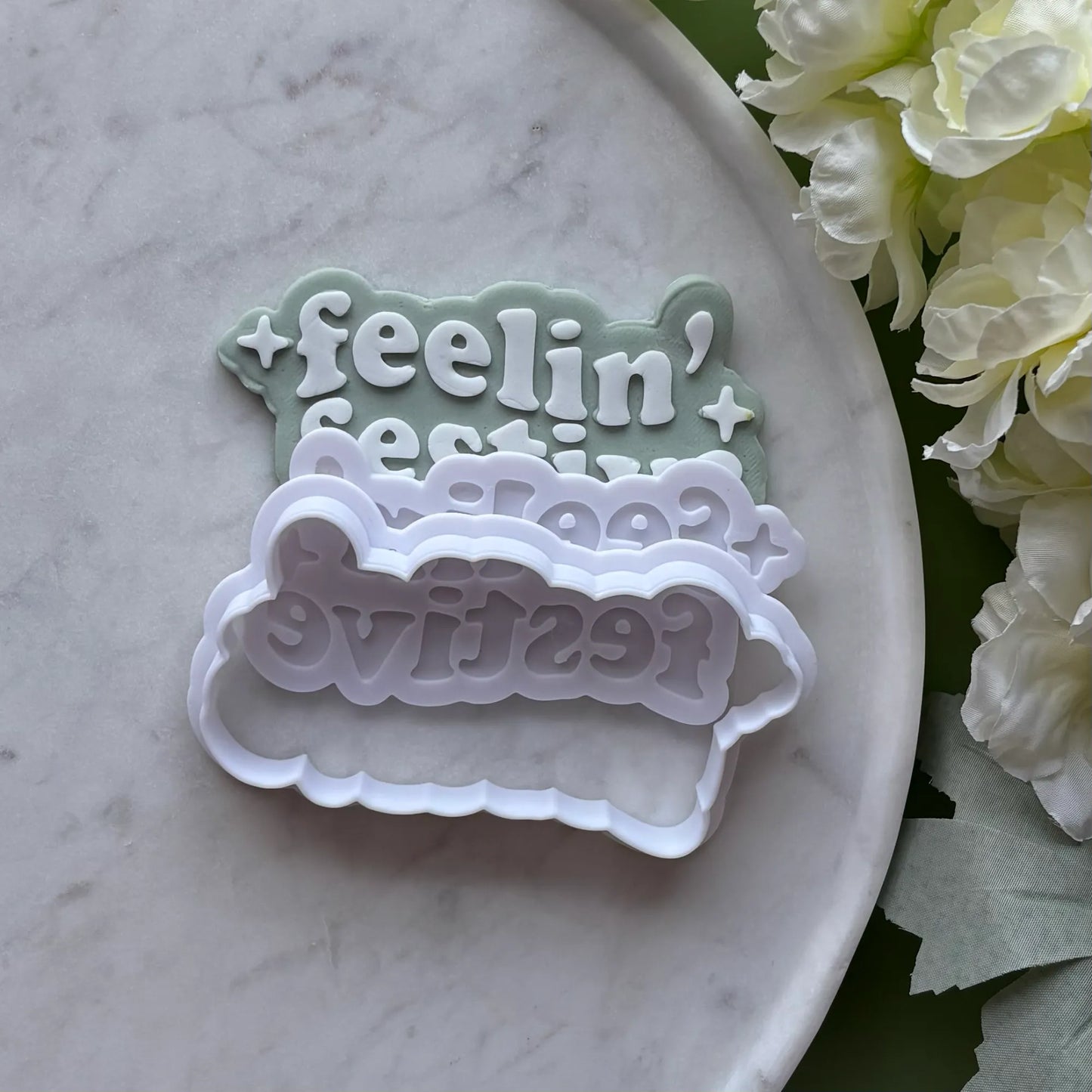 ‘Feeling' Festive' stamped onto Green fondant using a cookie cutter and debosser, displayed on a marble surface