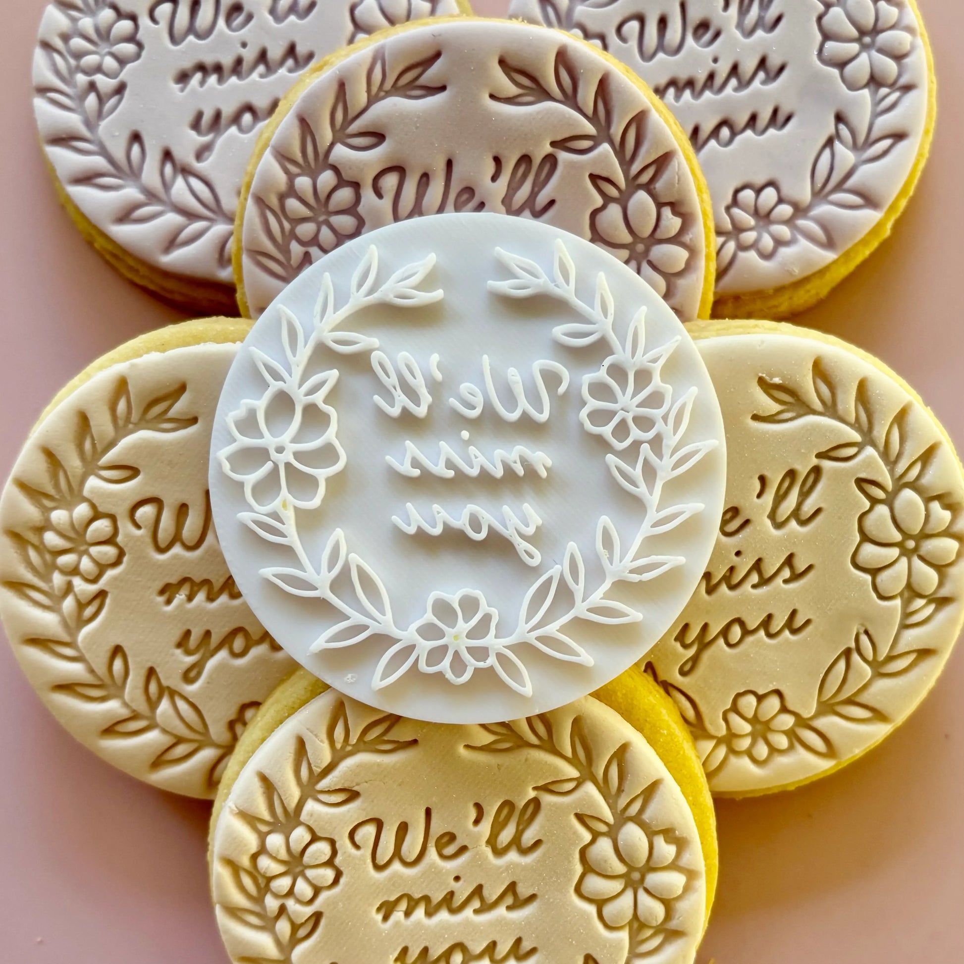 Decorative cookies with 'We'll miss you' text and floral designs on a pink background