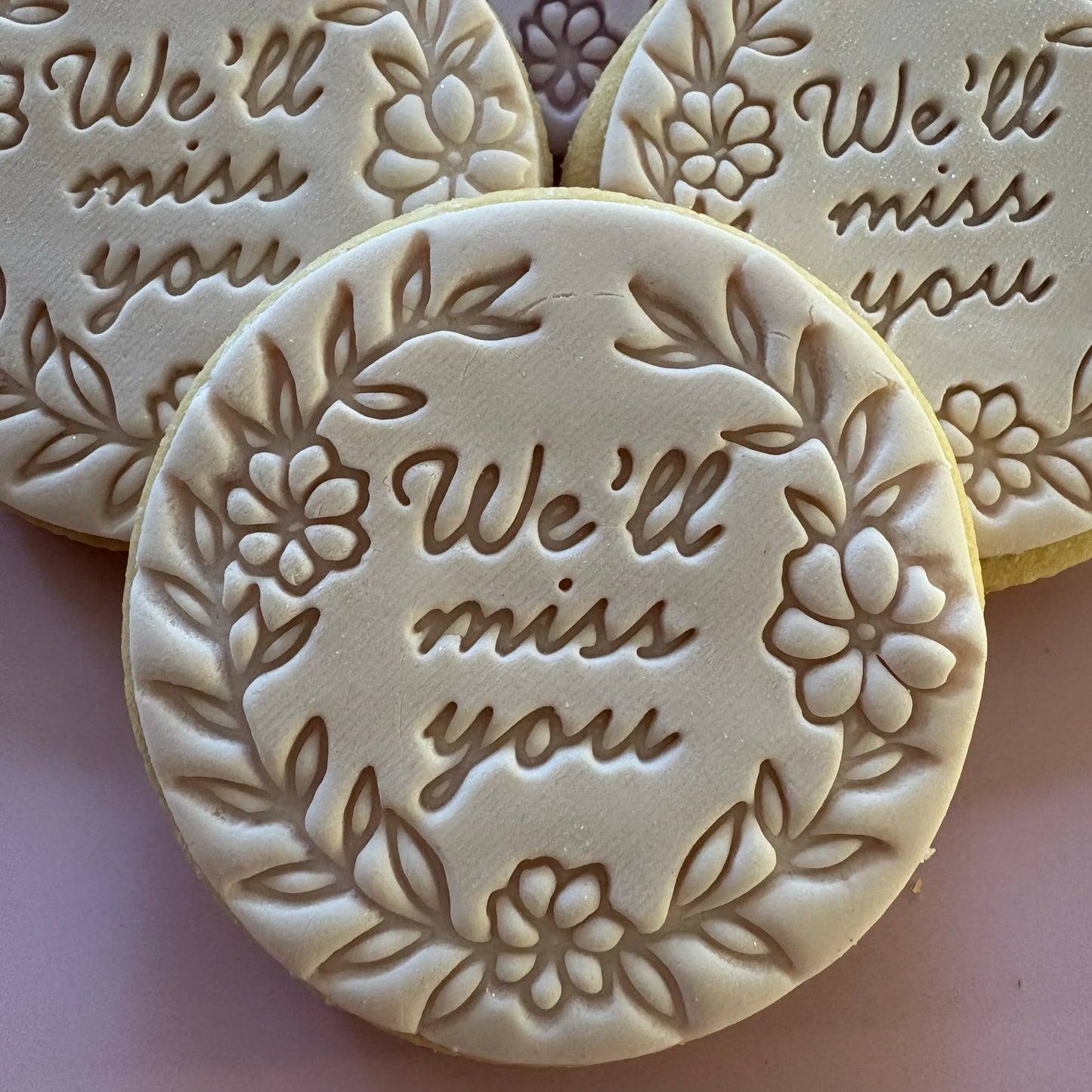 Round cookies with 'We'll miss you' text and floral designs on a light pink background