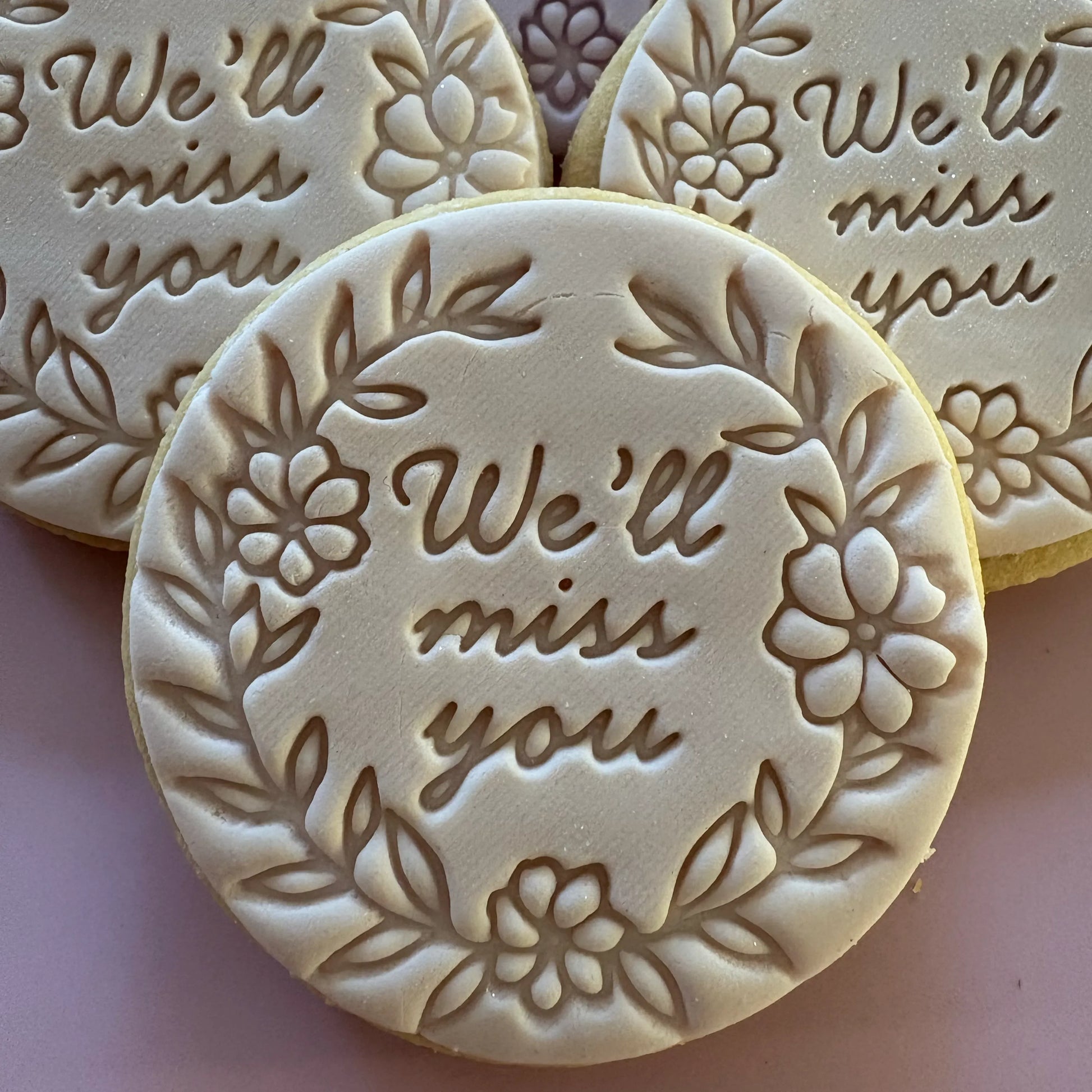 Round cookies with 'We'll miss you' text and floral designs on a light pink background