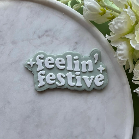 ‘Feeling' Festive' stamped onto Green fondant using a cookie cutter and debosser, displayed on a marble surface.