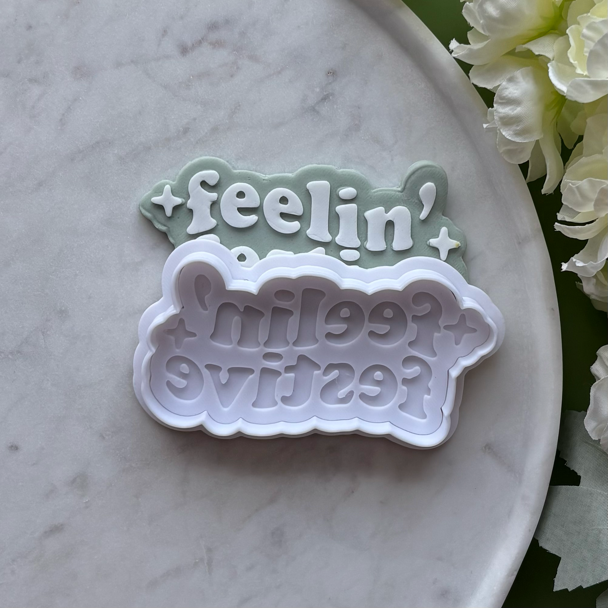 ‘Feeling' Festive' stamped onto Green fondant using a cookie cutter and debosser, displayed on a marble surface.