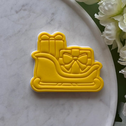 Yellow sled cookie cutter with a bow on a marble surface with flowers.