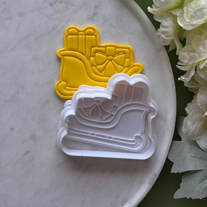 Set of cookie cutters shaped like a sleigh with a bow on a marble surface.