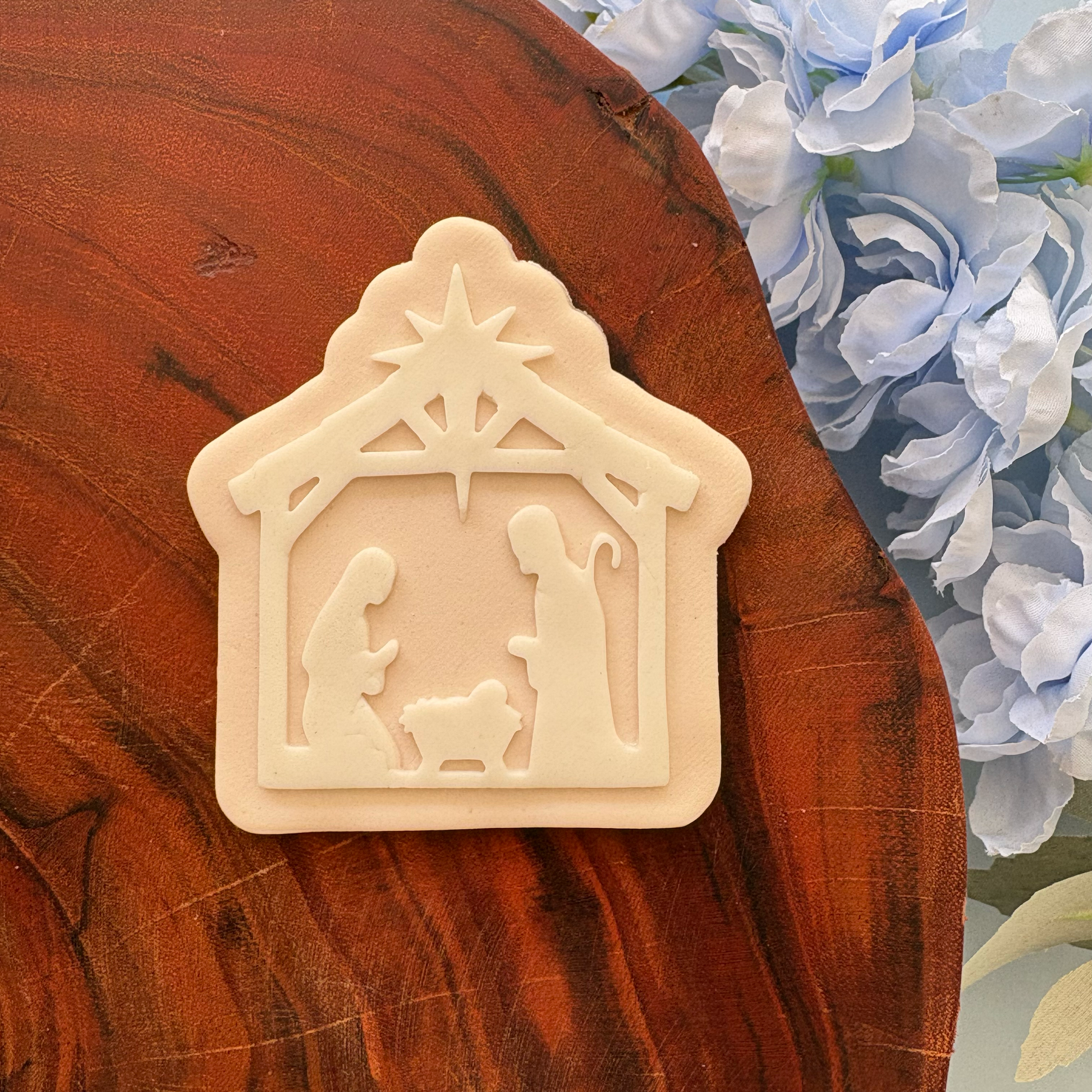 Decorative nativity scene on a wooden surface with flowers in the background