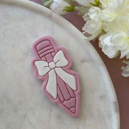 Pink and white decorative item resembling a bottle with a bow on a marble surface with flowers in the background.