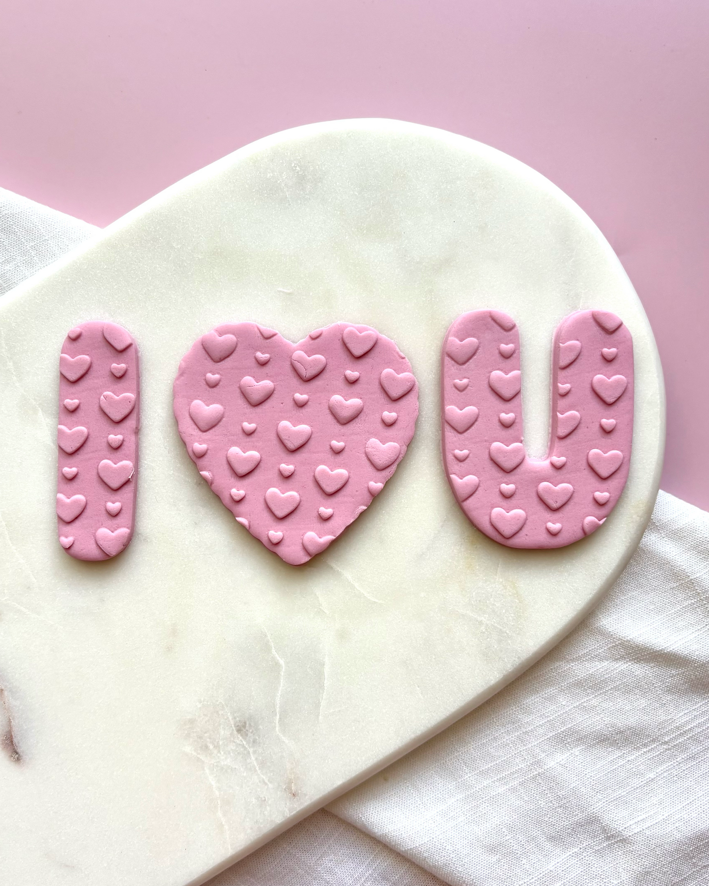 Pink 'I ❤️ U' cookie cutters on a marble surface with a pink background