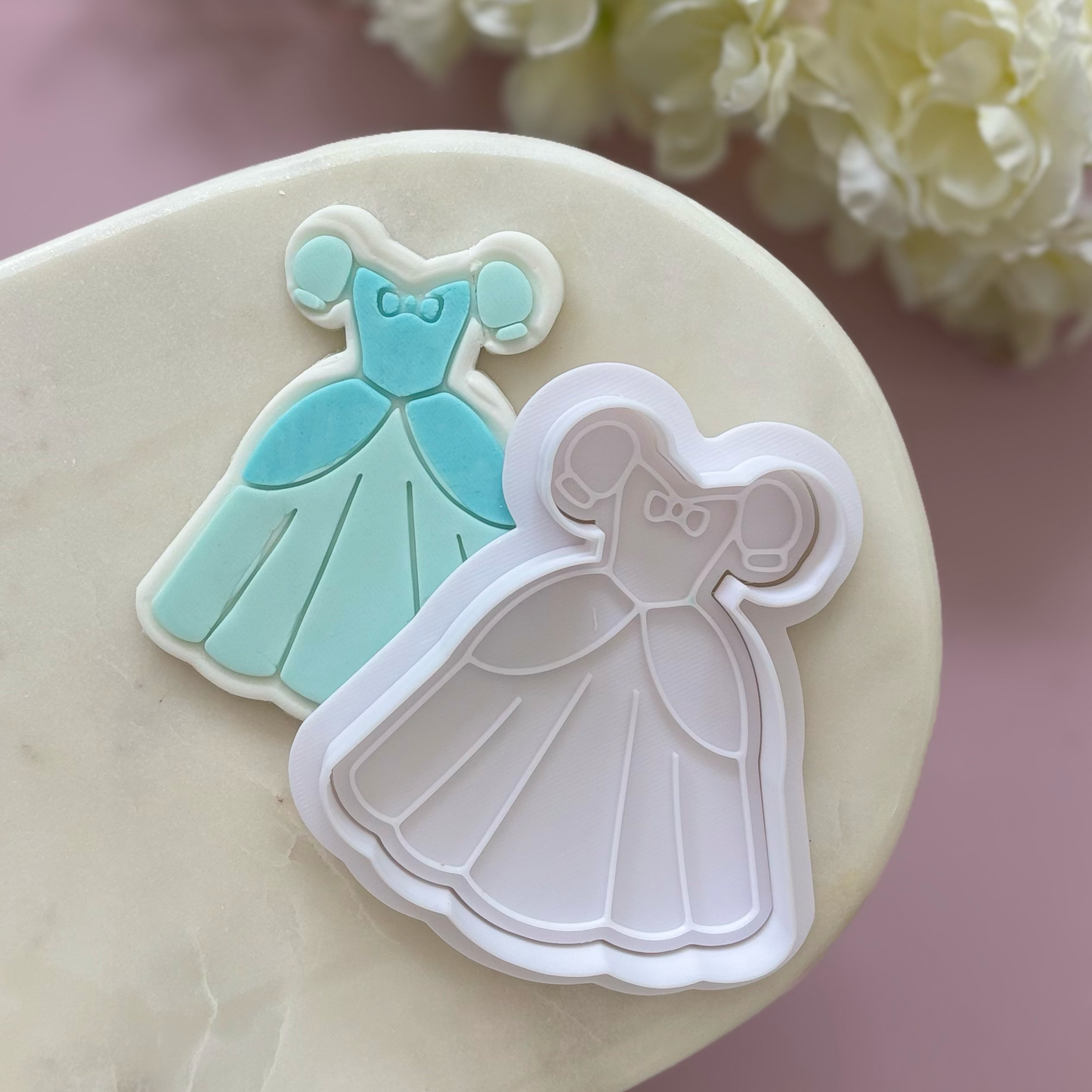 Cookie cutters shaped like dresses on a marble surface with flowers in the background