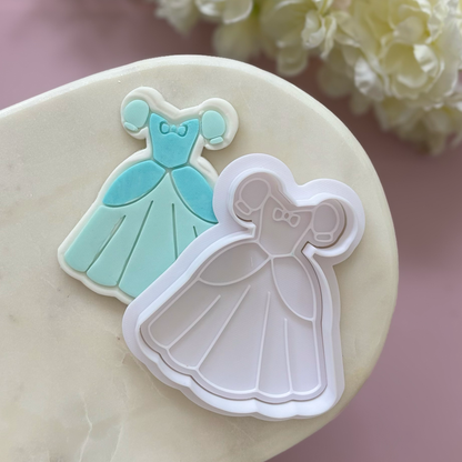 Cookie cutters shaped like dresses on a marble surface with flowers in the background