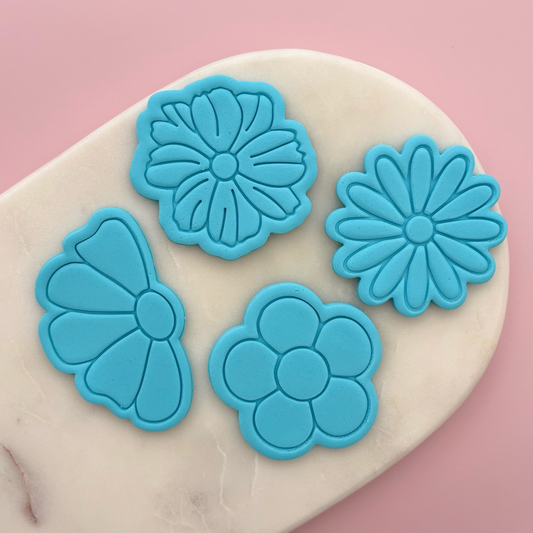 Blue flower-shaped cookie cutters on a marble surface with a pink background