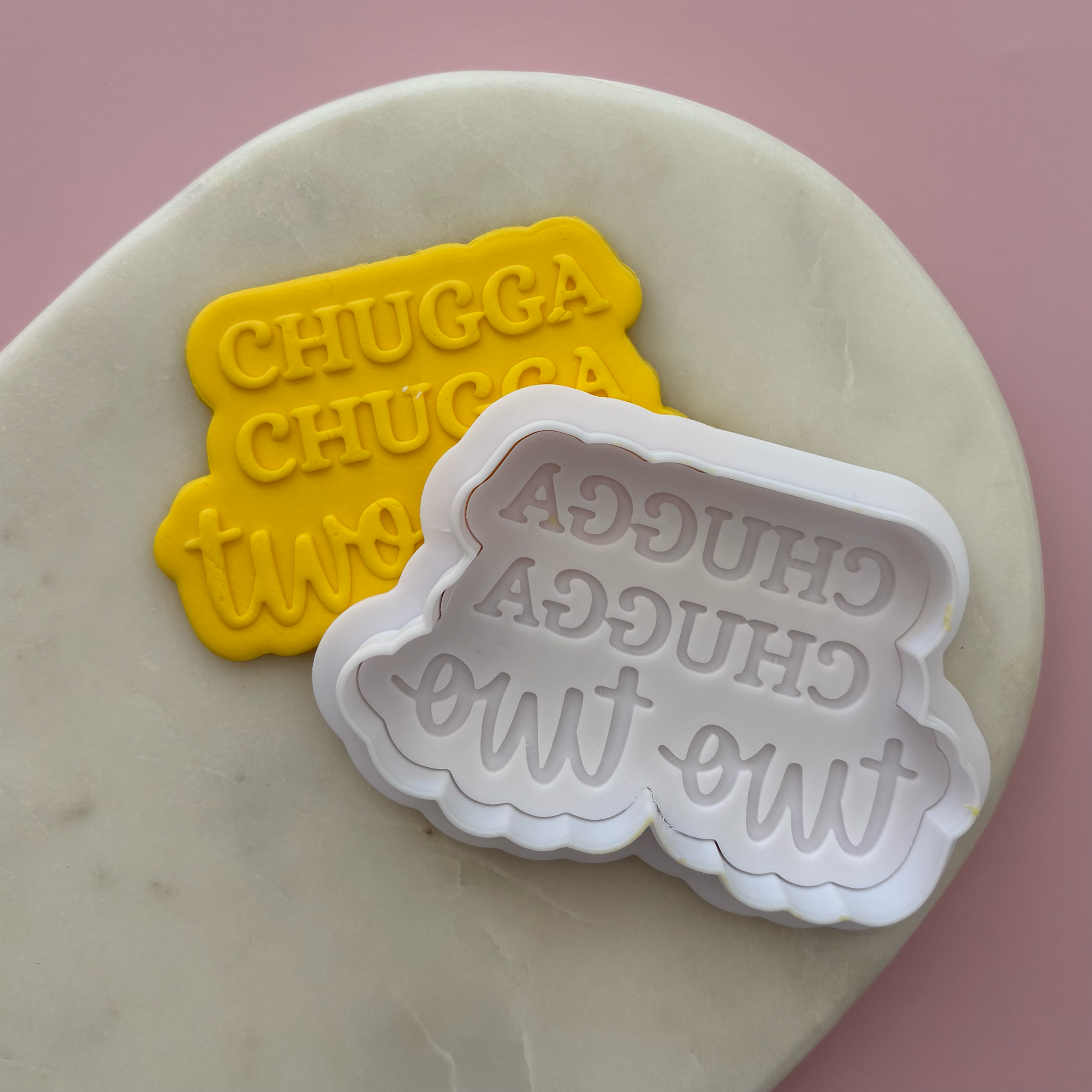 Two cookie cutters with 'CHUGGA CHUGGA two two' text on a marble surface.