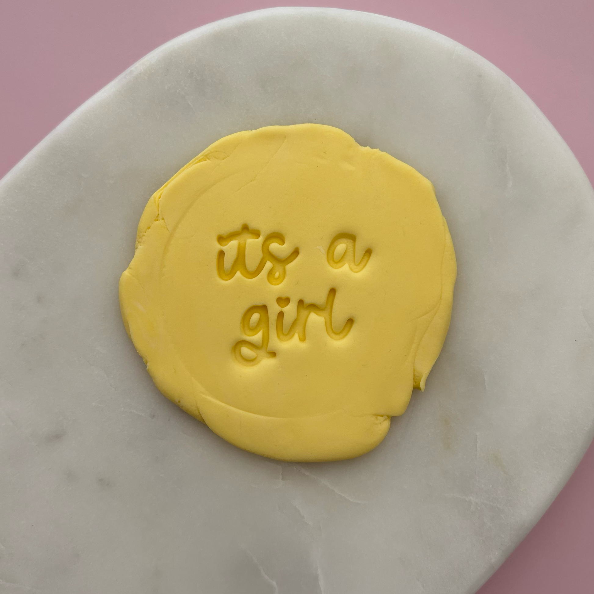 Yellow fondant with 'it's a girl' text on a marble surface
