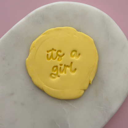 Yellow fondant with 'it's a girl' text on a marble surface