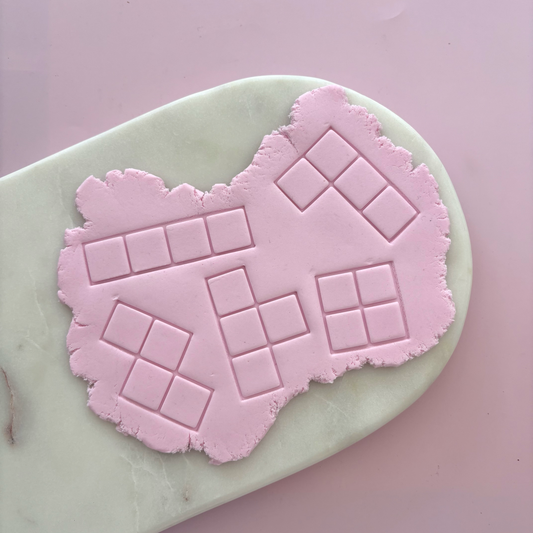 A pink silicone baking mat with embossed square grid patterns, shown on a pale green marble board against a solid pink background.