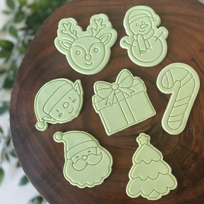 A set of green Christmas-themed cookie cutters and fondant embossers on a wooden surface.