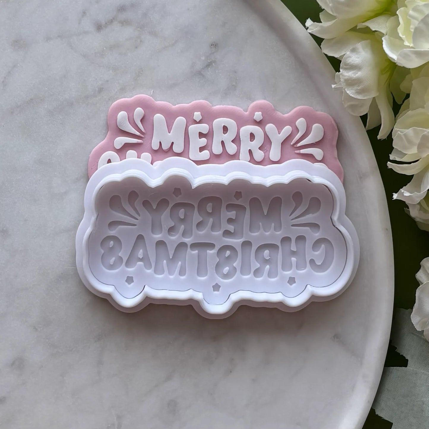 ‘Merry Christmas’ stamped onto pink fondant using a cookie cutter and debosser, displayed on a marble surface