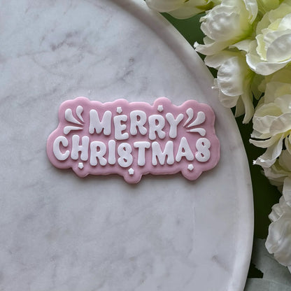 ‘Merry Christmas’ stamped onto pink fondant using a cookie cutter and debosser, displayed on a marble surface