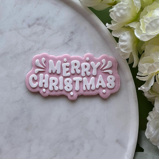 ‘Merry Christmas’ stamped onto pink fondant using a cookie cutter and debosser, displayed on a marble surface
