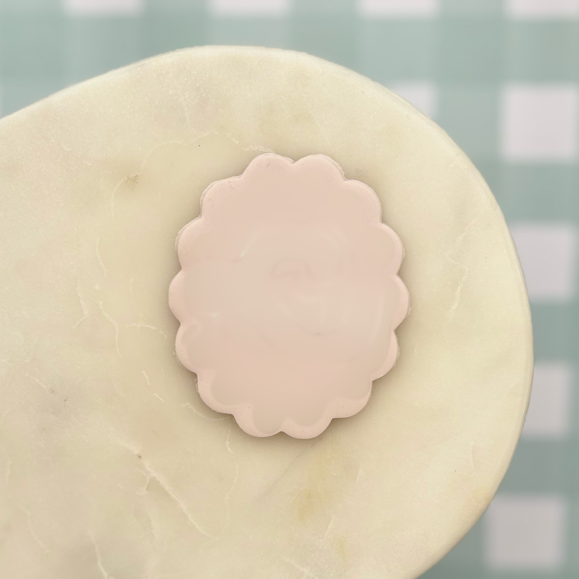 Pink scalloped-edge decorative element on a beige surface with a light green checkered background