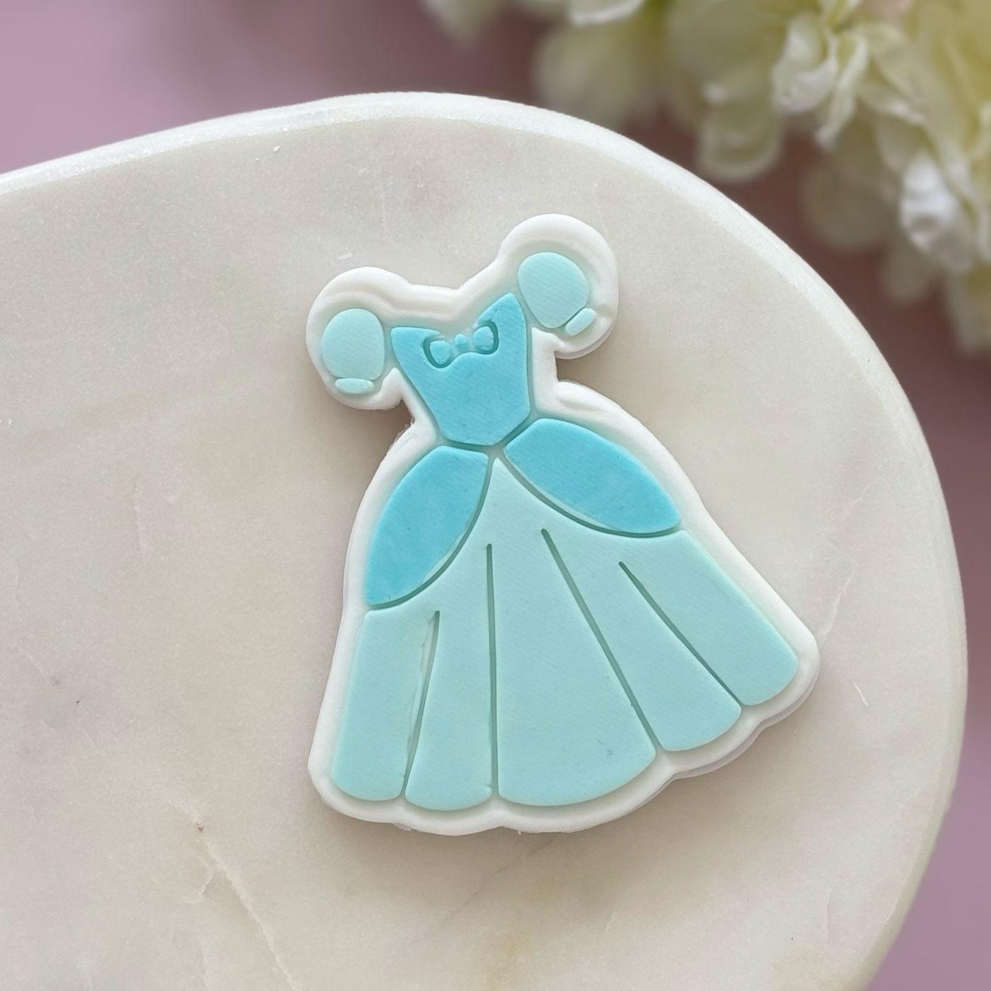 Blue dress-shaped cookie on a white plate with a blurred floral background