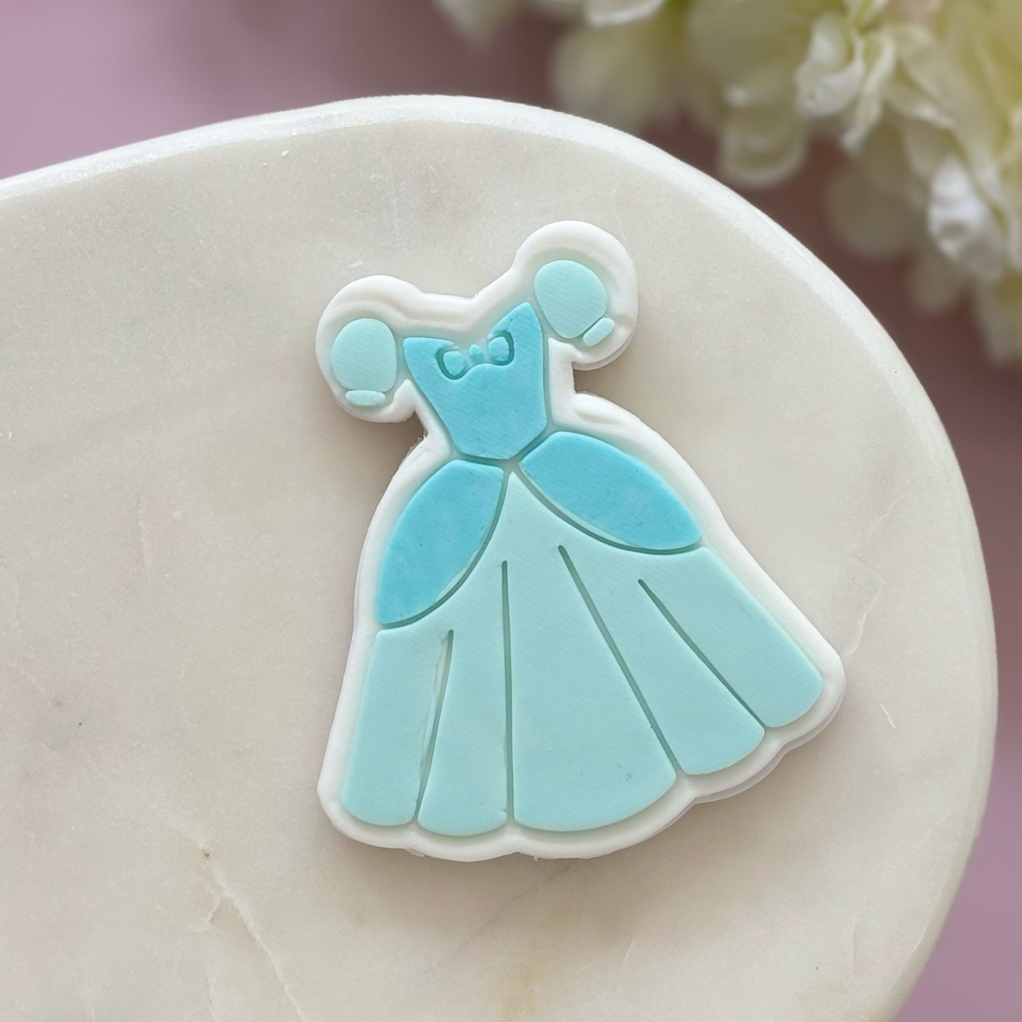Blue dress-shaped cookie on a white plate with a blurred floral background