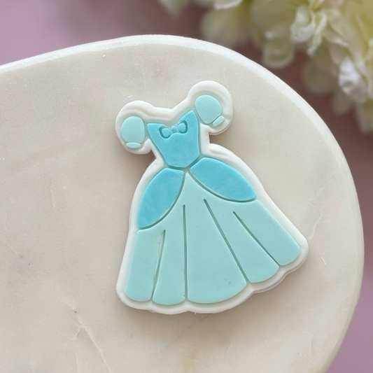 Blue dress-shaped cookie on a white plate with a blurred floral background
